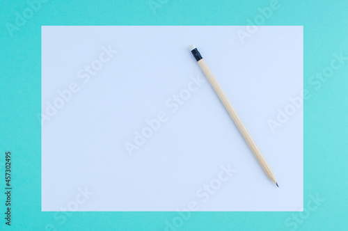 White sheet of paper and wooden pencil on turquoise background.