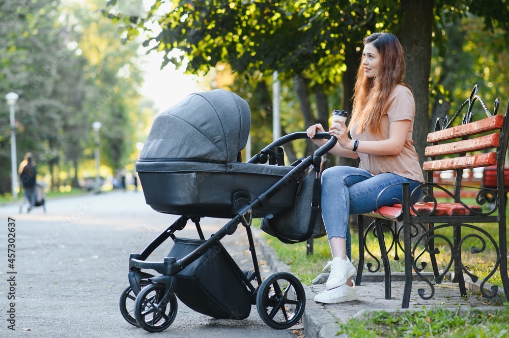 Mum sitting on a bench. Woman pushing her toddler sitting in a pram. Family concept. Mum sitting on a bench. Woman pushing her toddler sitting in a pram. Family concept.