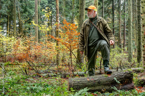 A hunter makes a stalking through his hunting grounds and climbs over a sawn tree trunk.