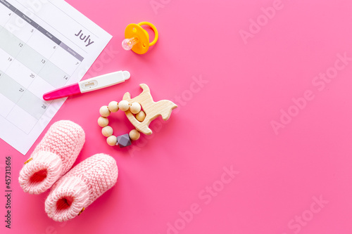 Pregnancy test with pink baby girl booties and calendar, top view