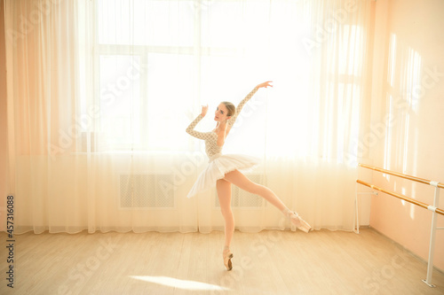 Fototapeta Naklejka Na Ścianę i Meble -  Beautiful ballerina in body and white tutu is training in a dance class. Young flexible dancer posing in pointe shoes.