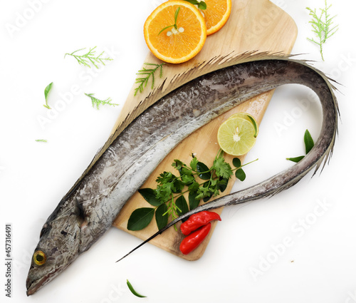 Fresh Largehead hairtail fish,Belt fish decorated with herbs and vegetables on a wooden pad.Selective focus. photo