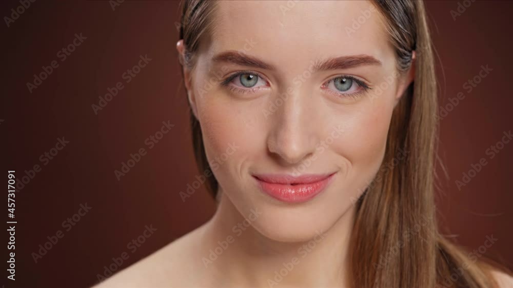Beautiful blue eyed woman smiles. Looks at the camera. Close-up on a brown background. High quality 4k footage Beautiful blue eyed woman smiles. Looks at the camera. Close-up on a brown background. High quality 4k footage