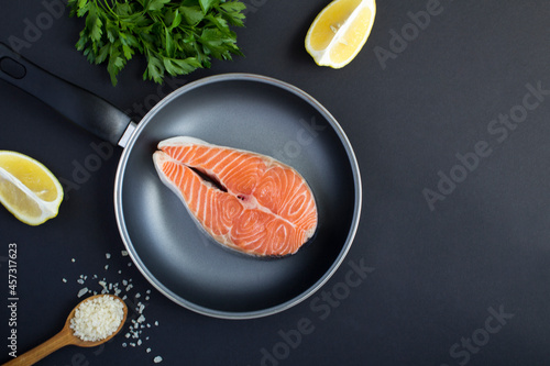 Top view of raw fish salmon in a frying pan on the black background. Close-up.Copy space.