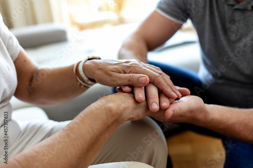 Man holding senior woman s hand at home. Male healthcare worker holding hands of senior woman at care home  focus on hands. Shot of a young man hands holding old senior elderly hand with love and care