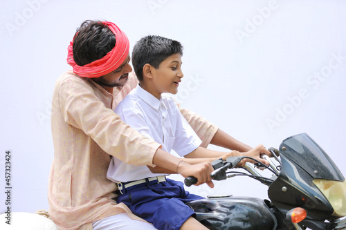 Young indian farmer dropping his child to school on bike.