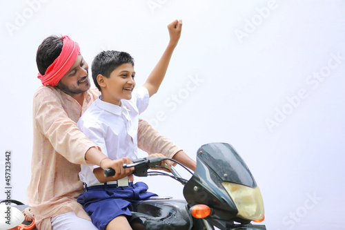 Young indian farmer dropping his child to school on bike.