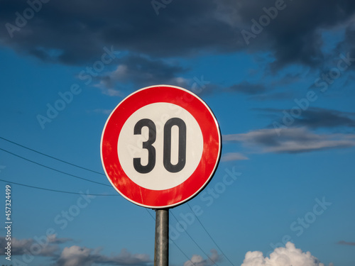 Metal road or traffic sign with number 30 in a red circle, indicating new speed limit against blue sky and clouds photo
