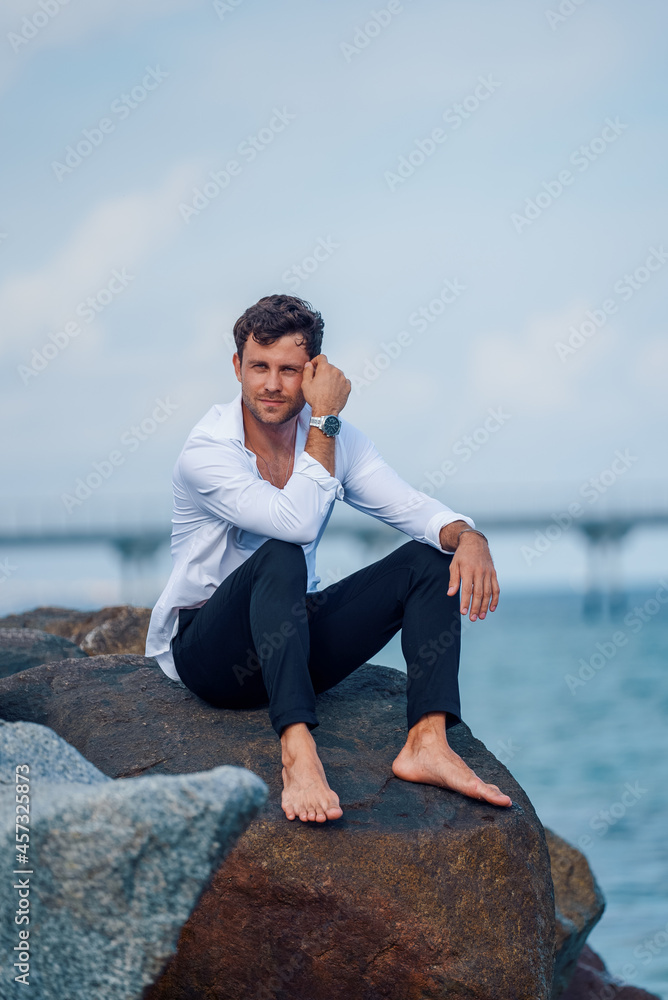 Content stylish man on rock near sea Content stylish man on rock near sea