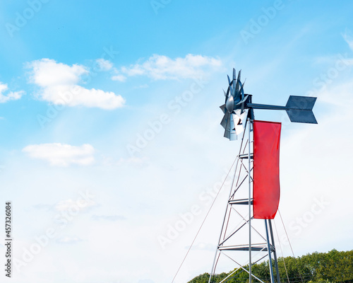 Windmill weather vane with red flag on blue sky background