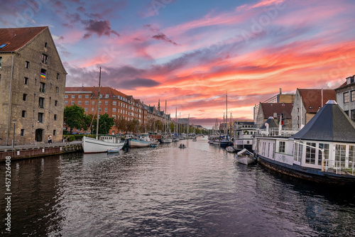 Beautiful canals of Copenhagen, the capital of Denmark. Magical summer view of Copenhagen city narrow streets, buildings, pedestrian bridges and boats down the canals at sunset.