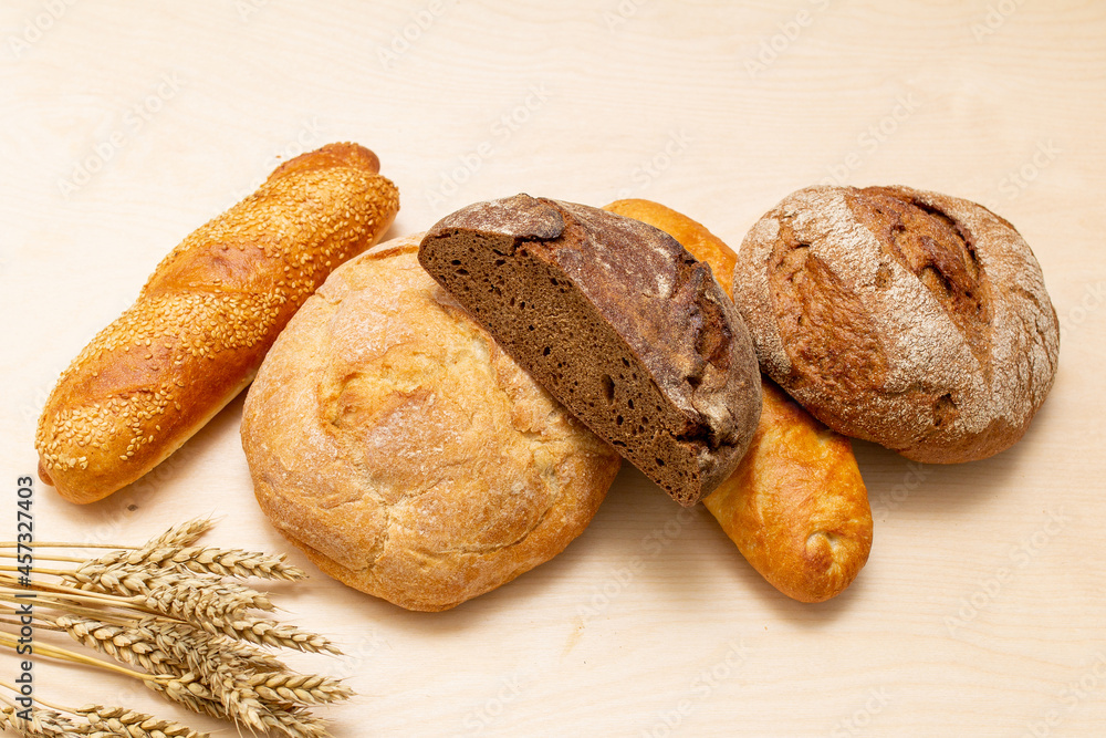 bread and wheat on the table, loaves of assorted freshly baked bread on a stone background
