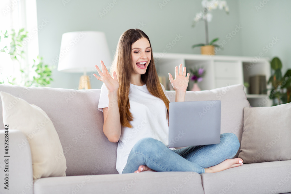 Portrait of attractive cheerful lucky girl sitting on divan using laptop having fun at home living room indoors Portrait of attractive cheerful lucky girl sitting on divan using laptop having fun at home living room indoors
