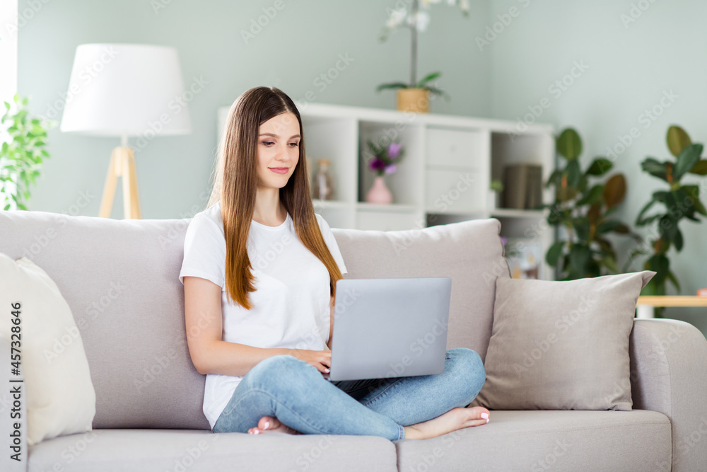 Portrait of attractive focused girl sitting on divan using laptop typing e-mail staying at home indoors Portrait of attractive focused girl sitting on divan using laptop typing e-mail staying at home indoors