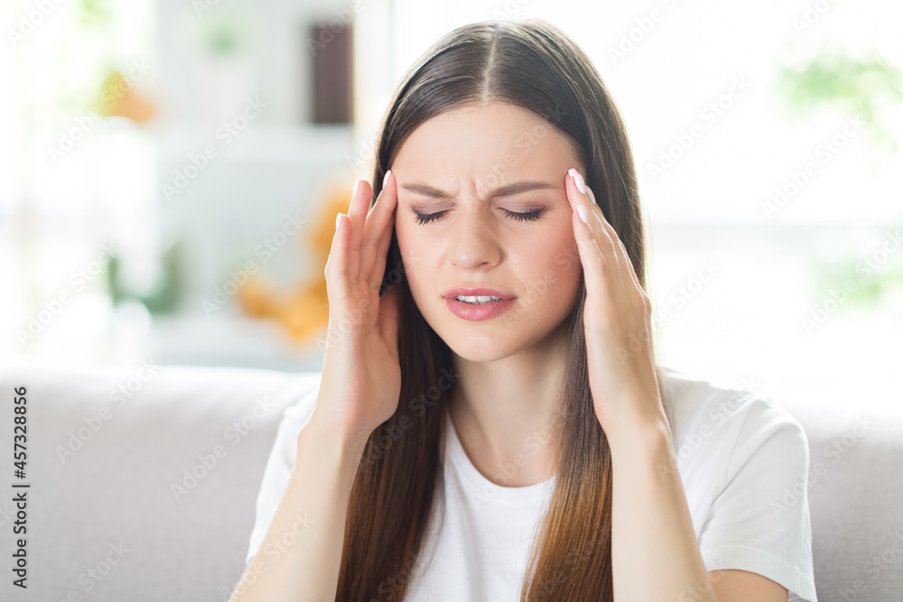 Portrait of attractive depressed frustrated brown-haired girl touching temple feeling bad at home indoors Portrait of attractive depressed frustrated brown-haired girl touching temple feeling bad at home indoors