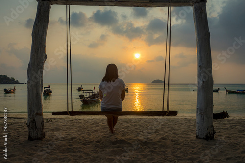 A woman sitting on a swing watching the sunrise alone