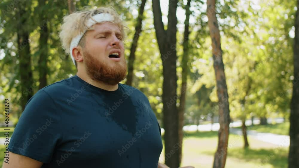 Tired obese man jogging, then taking break, drinking water and washing face during fat burning workout in park Tired obese man jogging, then taking break, drinking water and washing face during fat burning workout in park