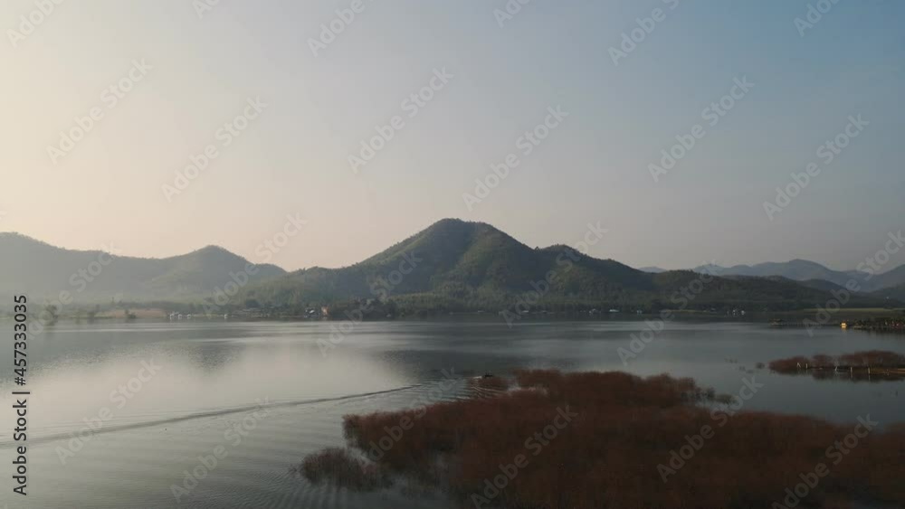 Scenery of Lam Thaphoen reservoir with mountain range and traditional long-tail boat sailing in the morning at Suphanburi Scenery of Lam Thaphoen reservoir with mountain range and traditional long-tail boat sailing in the morning at Suphanburi