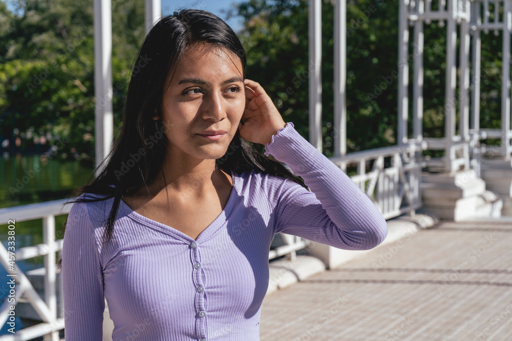 Young latin woman fixing her hair and standing on an old pedestrian bridge.
