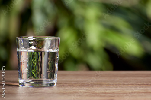 glass tumbler full of water on wooden table and natural background