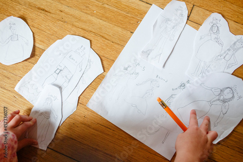 Close-up view of small child drawing paper dolls with a pencil photo