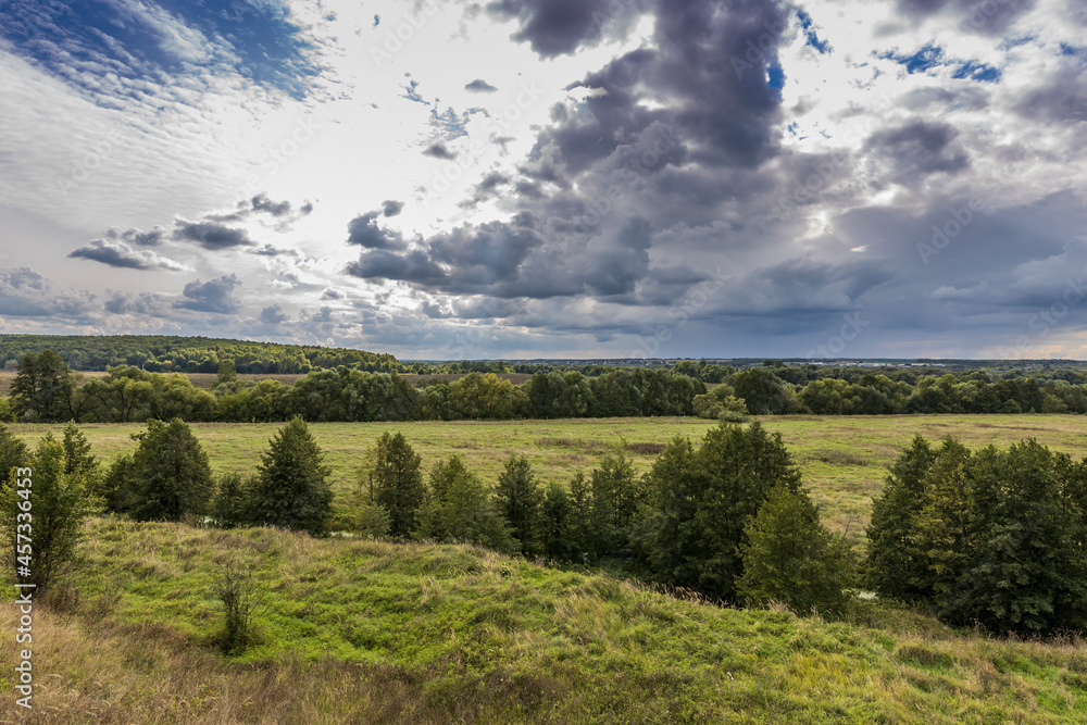 Summer field and clouds on the blue sky. A landscape with a bright green field and dramatic clouds against a blue sky.