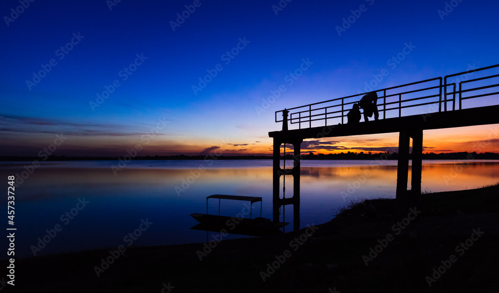 Two silhouette people on the bridge with a sunset background and a boat Two silhouette people on the bridge with a sunset background and a boat