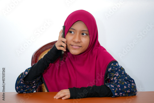 A young female muslim teenager wearing hijab is studying isolated on white background © laboostudio