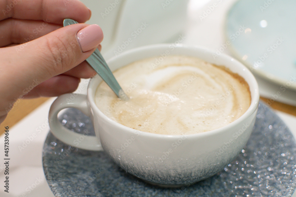 Girl mixes sugar with a spoon in a beautiful cup of fresh coffee. Breakfast at the cafe. Girl mixes sugar with a spoon in a beautiful cup of fresh coffee. Breakfast at the cafe.