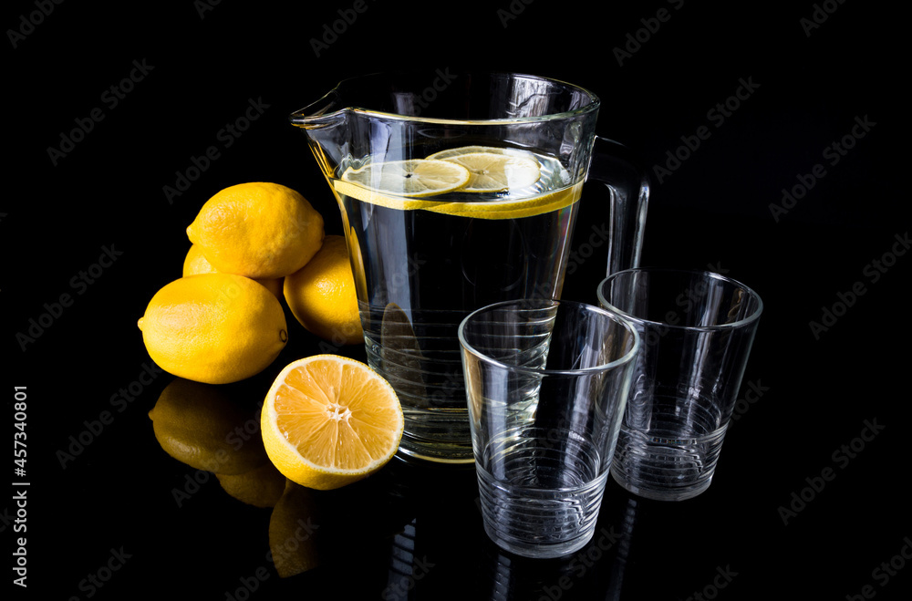 Jug or pitcher of water with lemons and two empty glasses, on black background. Jug or pitcher of water with lemons and two empty glasses, on black background.