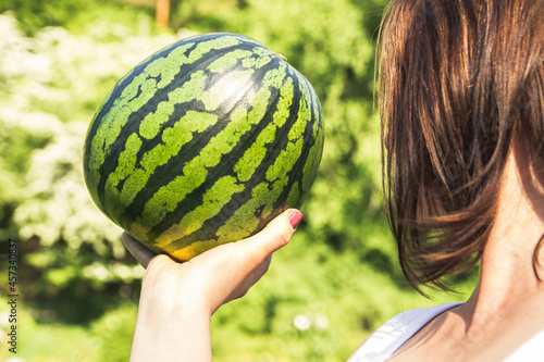 Young girl holding whole watermelon on a sunny summer day.