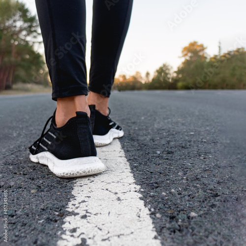 runlegs of a young woman in black sneakers prepare for a run on the road along the markings healthy lifestyle morning jogging on the road 