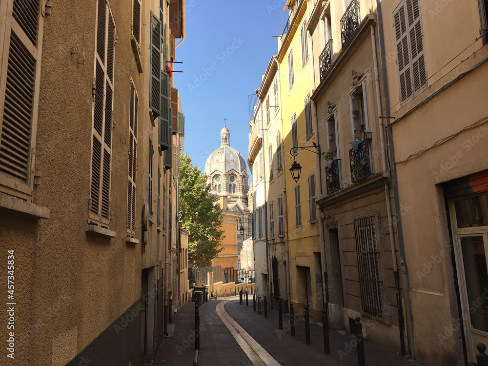 Pastel coloured residential buildings on a calm and friendly street with the Marseille Cathedral (Cathédrale de la Major) in the background, in Le Panier - Marseille's oldest neighborhood.