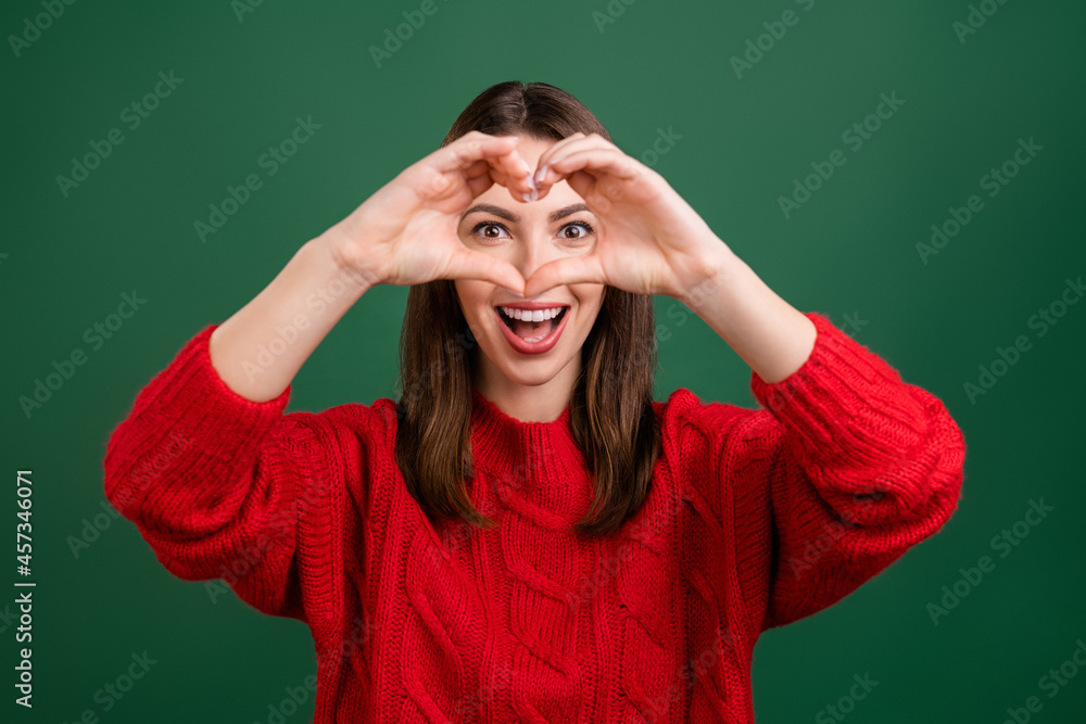 Photo portrait girl in red pullover showing heart shaped sign fingers smiling isolated green color background Photo portrait girl in red pullover showing heart shaped sign fingers smiling isolated green color background