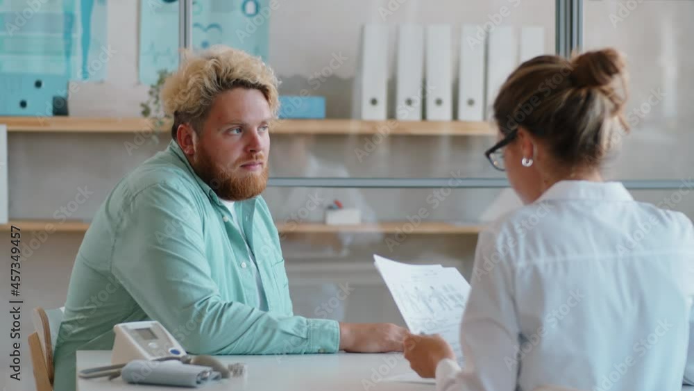 Young overweight man giving medical history to female doctor, smiling and speaking with her during healthcare consultation in clinic Young overweight man giving medical history to female doctor, smiling and speaking with her during healthcare consultation in clinic