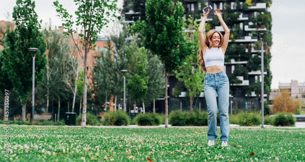 Young caucasian woman dancing outdoor feeling free and celebrating enjoying music using smartphone - advertising banner