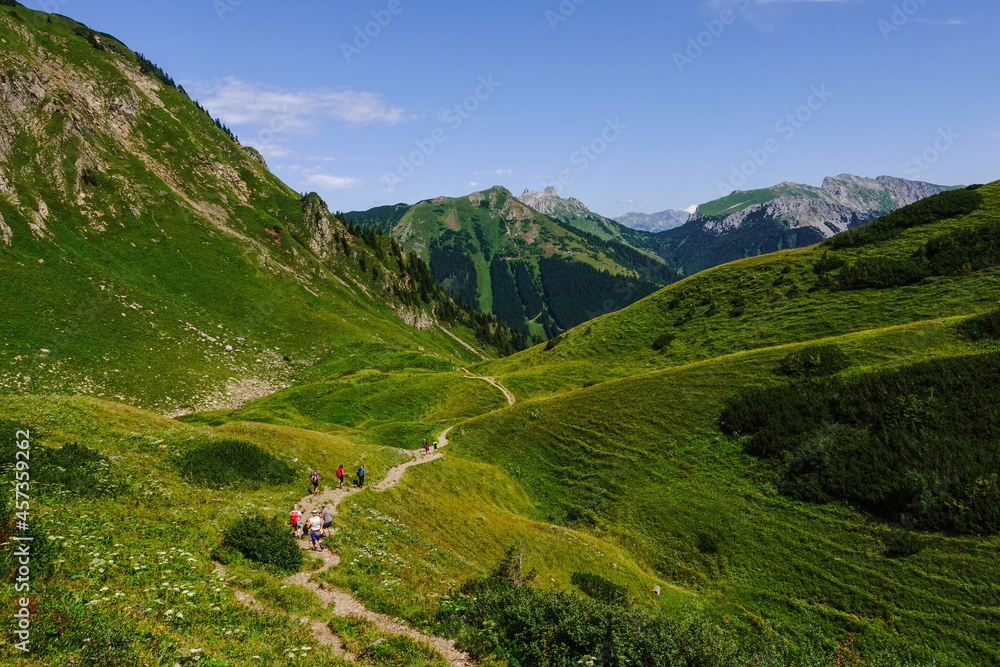 long hiking path in a green mountain landscape with colorful hikers