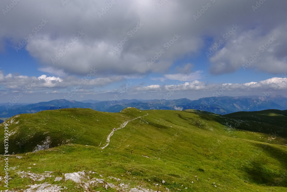 long hiking path on the top from a green mountain with grey clouds on blue sky long hiking path on the top from a green mountain with grey clouds on blue sky