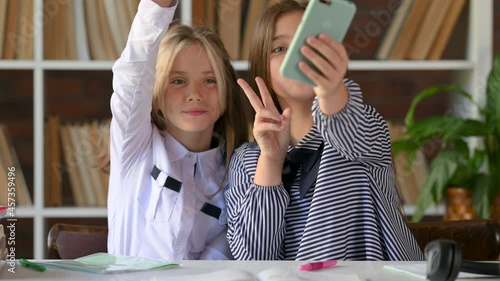 Two female students sitting at a desk use a smartphone take a selfie