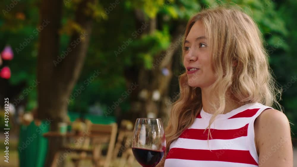 A close up shot of a very attractive white woman with wavy blonde hair, she s holding a wine glasses and giggling while she is at an outside cafe. Shot on ARRI Alexa Mini. A close up shot of a very attractive white woman with wavy blonde hair, she s holding a wine glasses and giggling while she is at an outside cafe. Shot on ARRI Alexa Mini.