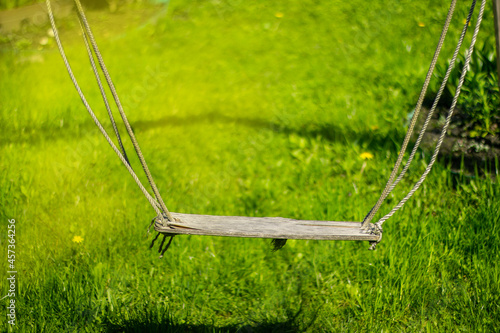 Old swing on ropes on a green background of grass lawn
