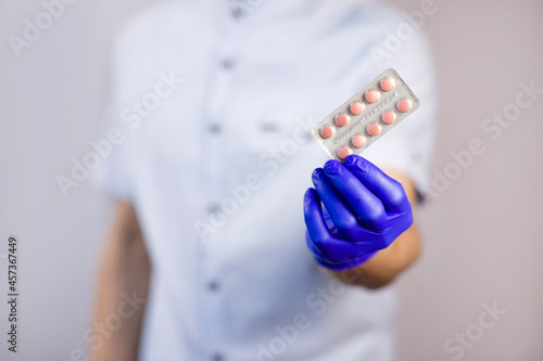 Doctor in gloves holds pills. Guy with protective gloves. Pink pills in hands. The guy holds out the pills. Treatment methods. Disease prevention. Health care.