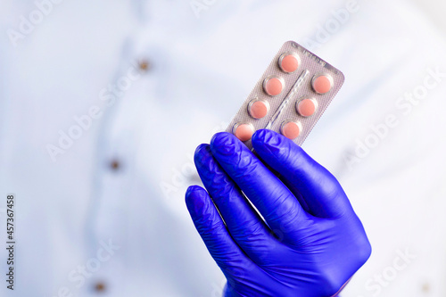 Doctor in gloves holds pills. Guy with protective gloves. Pink pills in hands. The guy holds out the pills. Treatment methods. Disease prevention. Health care.