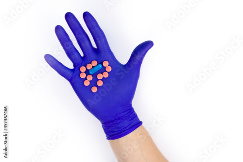 Hand in a protective glove on a white background. A man holds medicines in his hand.  Pills in hand on a white background. Pink pills. Treatment methods. Health care.