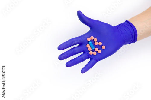 Hand in a protective glove on a white background. A man holds medicines in his hand.  Pills in hand on a white background. Pink pills. Treatment methods. Health care.