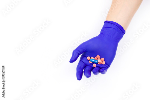 Hand in a protective glove on a white background. A man holds medicines in his hand.  Pills in hand on a white background. Pink pills. Treatment methods. Health care.