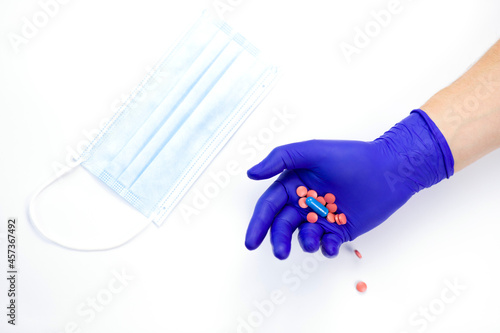 Pills in hand on a white background. Hand in a protective glove. Hand in a medical glove. Protective mask on the table. Virus protection. Medicines in hand. Vitamins to strengthen the immune system.