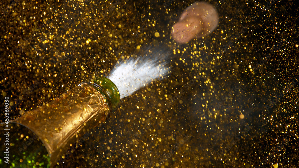 Freeze motion of Champagne explosion with flying cork closure, opening champagne bottle closeup, golden bokeh glitters on background.