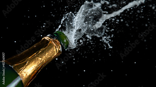 Freeze motion of Champagne explosion with flying cork closure, opening champagne bottle closeup isolated on black background. © Lukas Gojda