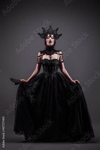 Foto Attractive young woman wearing a black dress, a crown and a fan